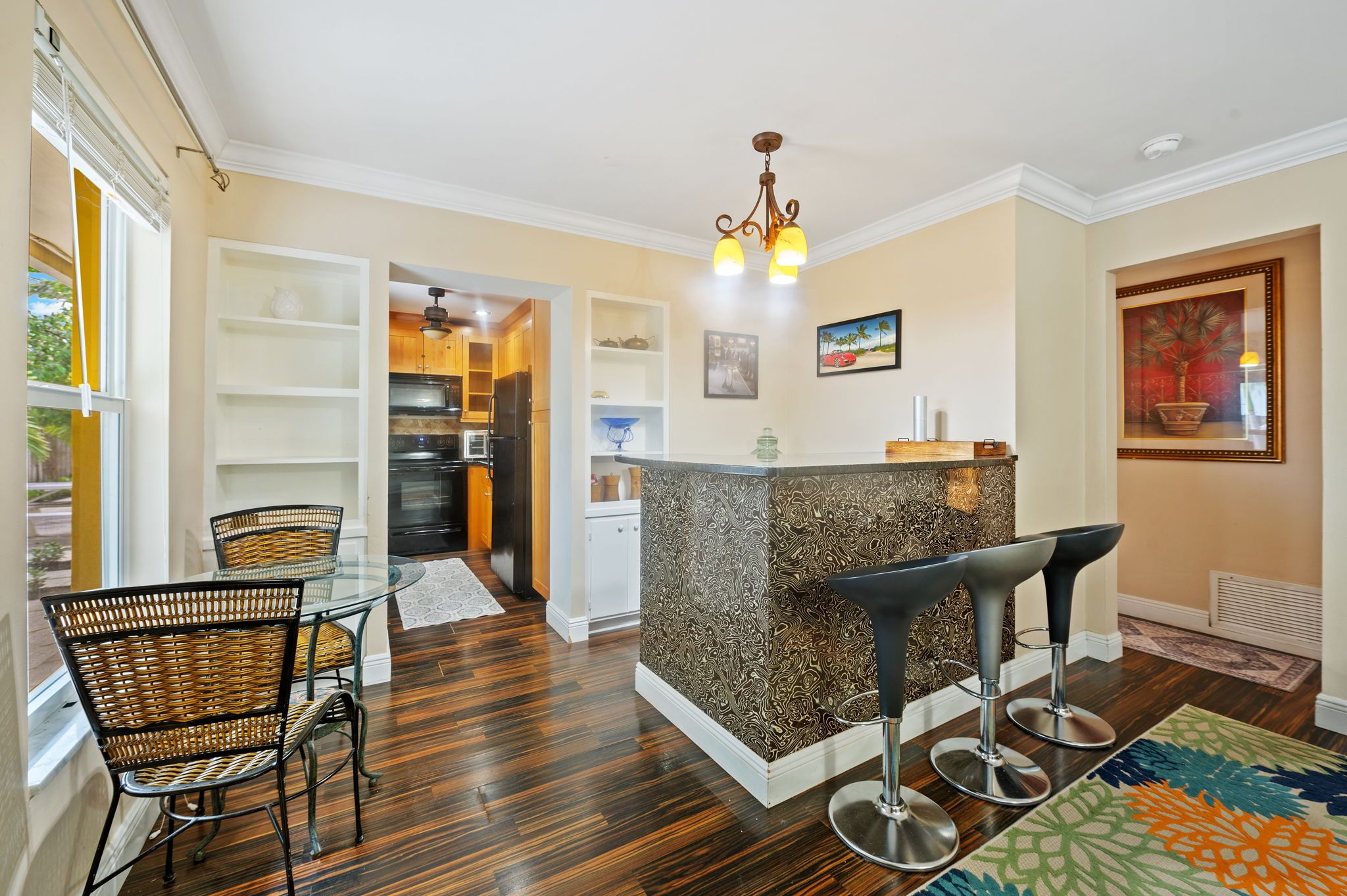 A modern kitchen with a central island, bar stools, and a dining area with wicker chairs.