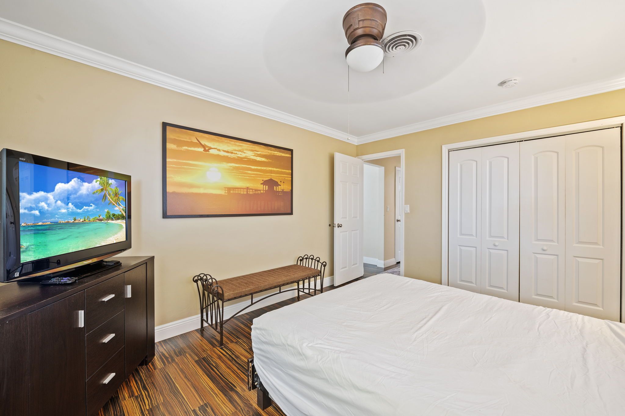 A hotel room with a bed, a desk, a television, and a painting of a sunset.