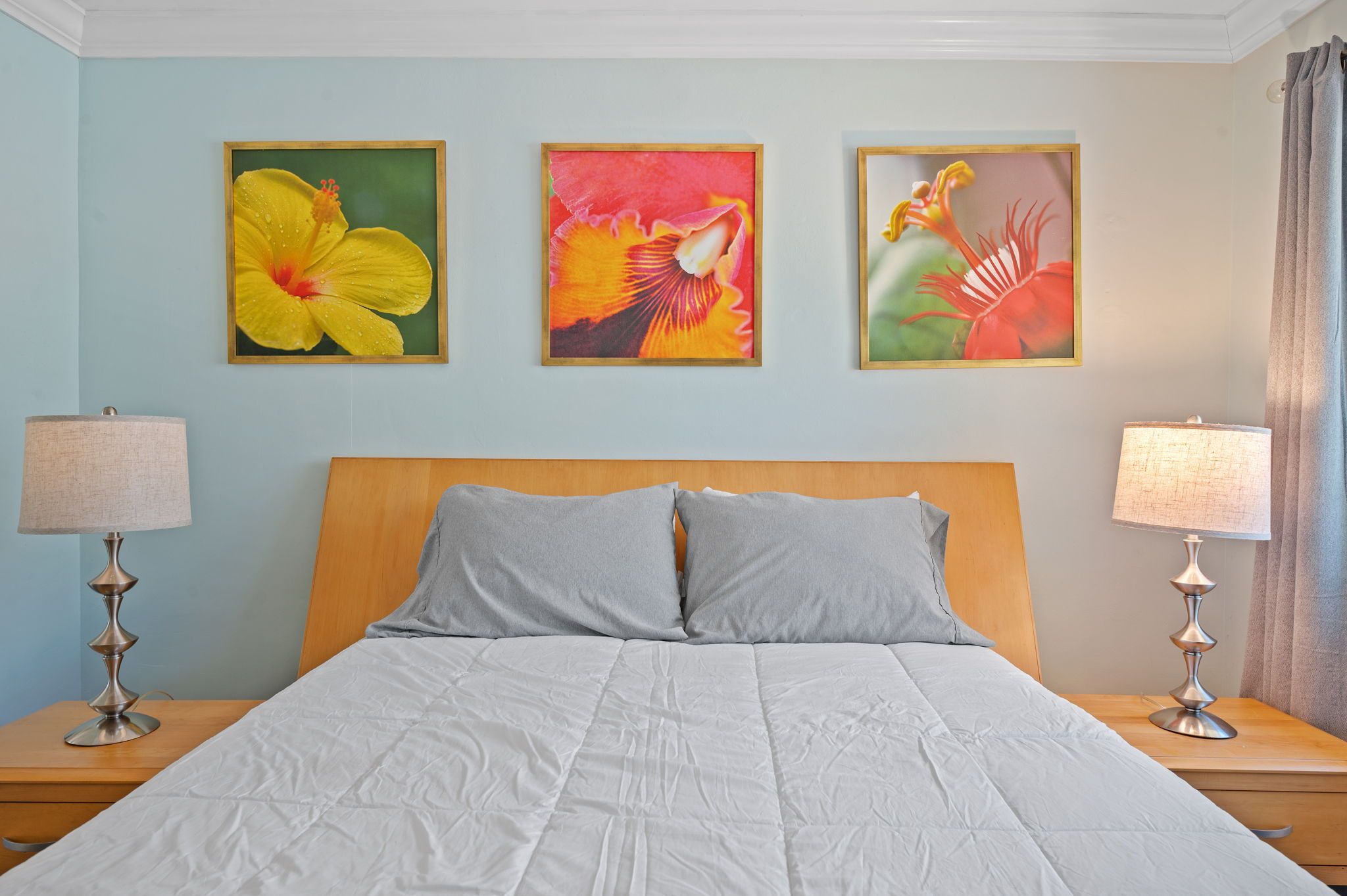 A bedroom with a bed, two nightstands, three wall-mounted paintings, and two lamps.