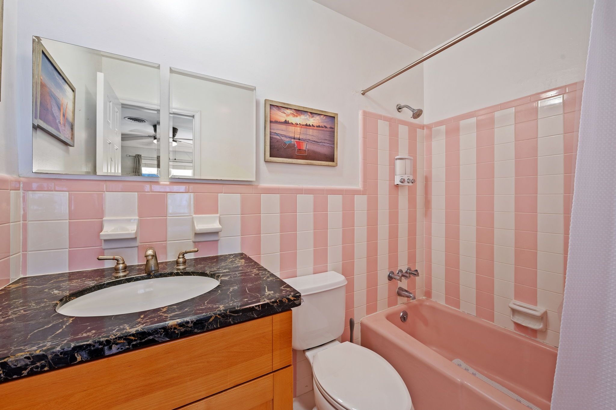 A bathroom with a marble sink, toilet, and pink-striped shower.