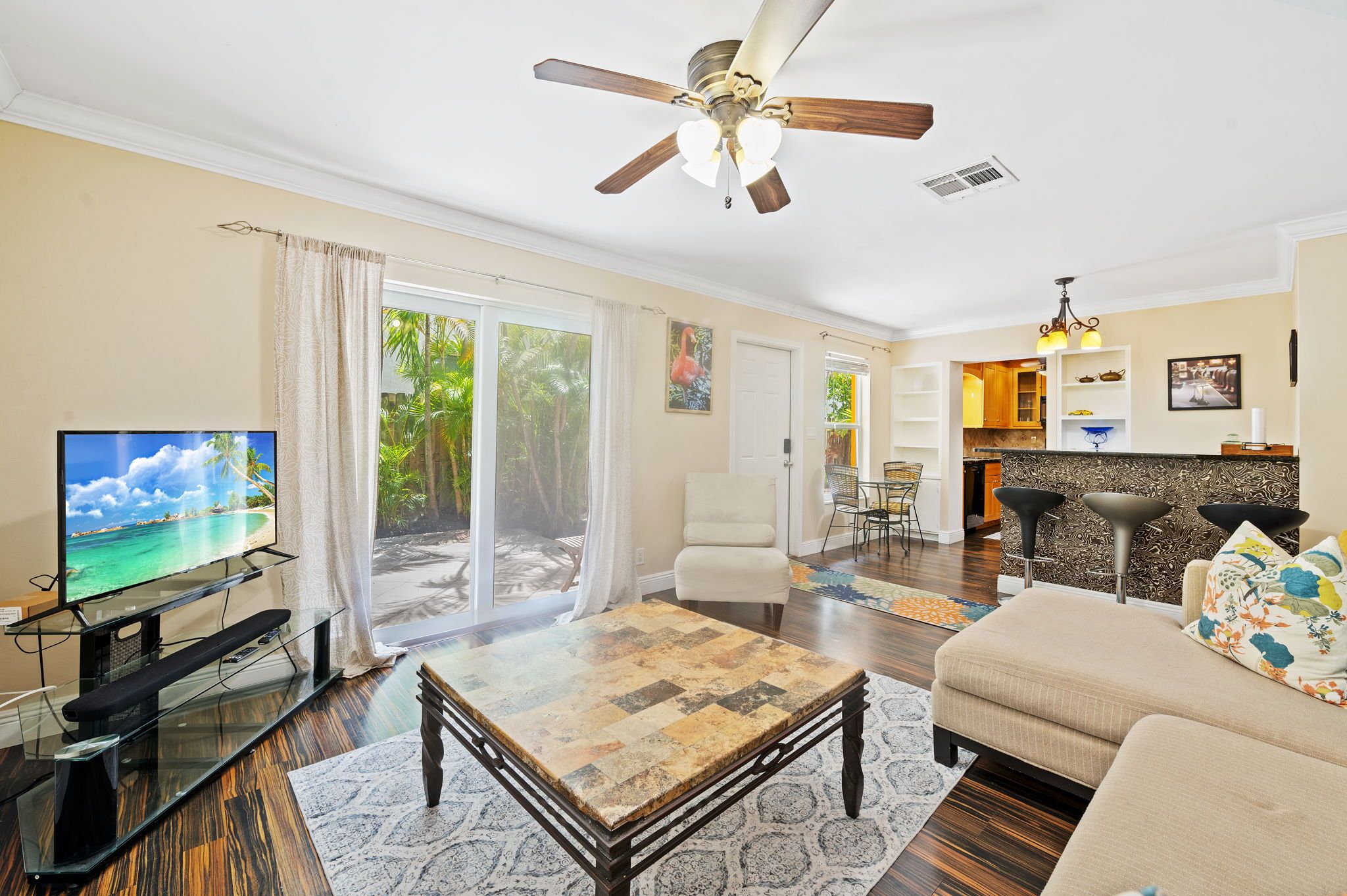 A living room with a television, a ceiling fan, a sofa, and a dining area with chairs.