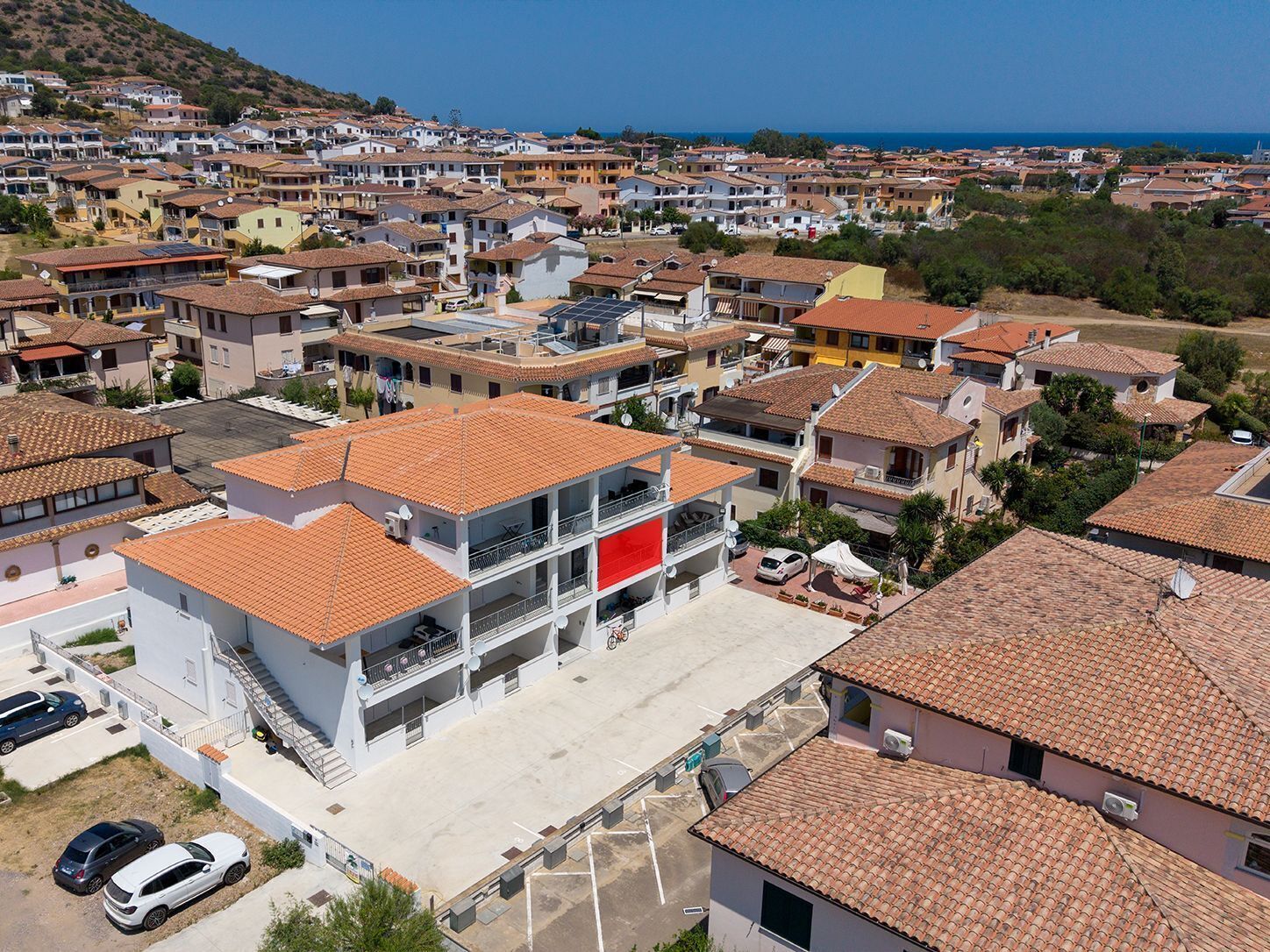 A residential area with multiple two-story buildings, a parking lot, and a clear view of the sea.