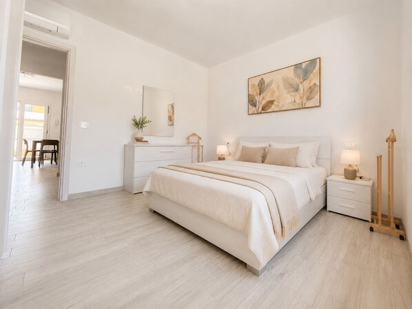 Ein Schlafzimmer mit Bett, Nachttischen, einem Schminktisch und einem Spiegel. An der Wand hängt ein Gemälde.