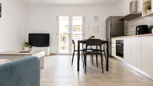 A modern kitchen with a dining area, a TV, and a view through a glass door. - Pegaso - Two Bedroom Apartment, Sleeps 5 (La Caletta)