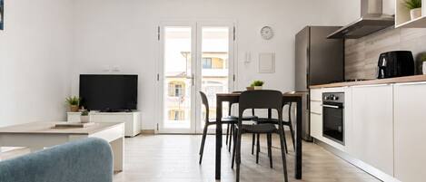 A modern kitchen with a dining area, a TV, and a view through a glass door.