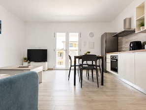 A modern kitchen with a dining area, a TV, and a view through a glass door. - Pegaso - Two Bedroom Apartment, Sleeps 5 (La Caletta)