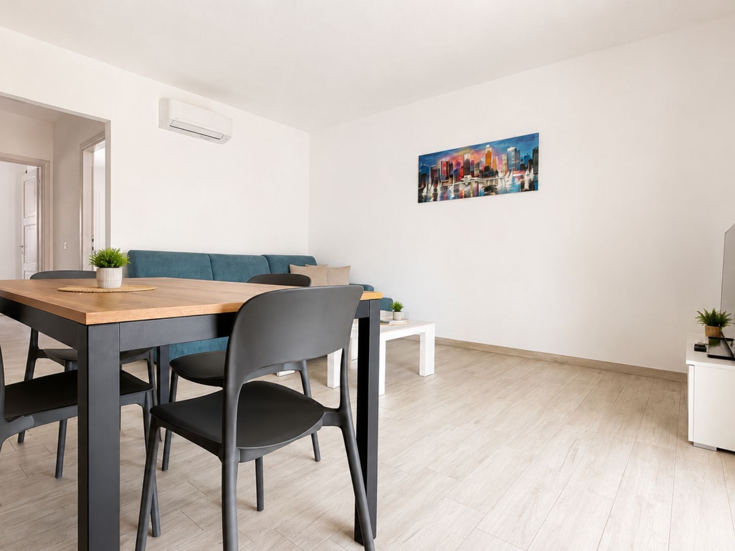 A modern living room with a dining area, a sofa, a coffee table, and a painting on the wall.