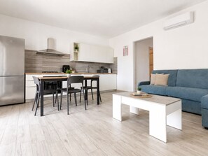A modern kitchen with white cabinets, a dining table with chairs, and a blue sofa in the living area. - Pegaso - Two Bedroom Apartment, Sleeps 5 (La Caletta)