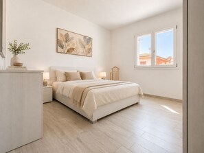 A bedroom with a bed, bedside tables, a nightstand, a window, and a wall-mounted artwork. - Pegaso - Two Bedroom Apartment, Sleeps 5 (La Caletta)