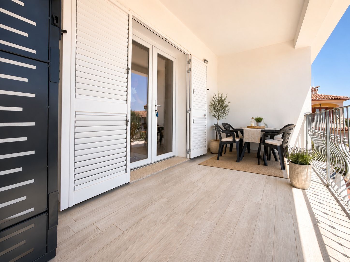 En balkon med et bord, stole og en potteplante, samt en skydedør.