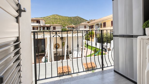 A balcony with a view of a courtyard, a mountain in the background, and a building with a tiled roof. - Pegaso - Two Bedroom Apartment, Sleeps 5 (La Caletta)