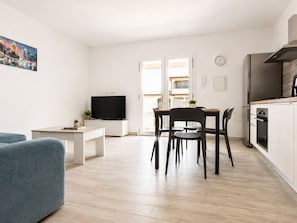 Ein modernes Wohnzimmer mit Flachbildfernseher, einem Essbereich mit Tisch und Stühlen sowie einer Küche mit Herd und Backofen.