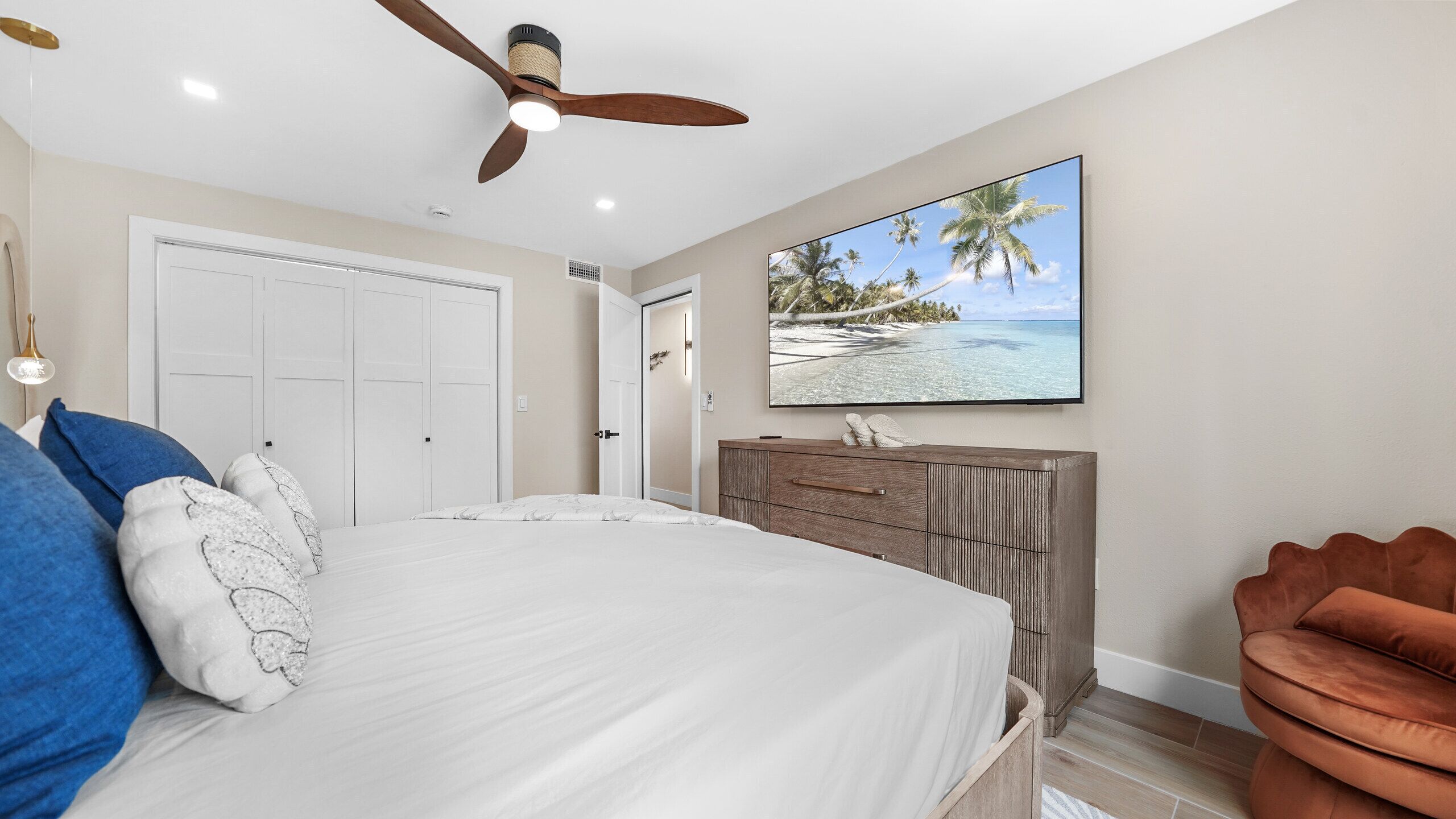 A bedroom with a bed, a ceiling fan, a wardrobe, and a television on the wall.