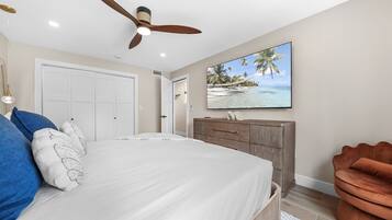 A bedroom with a bed, a ceiling fan, a wardrobe, and a television on the wall.