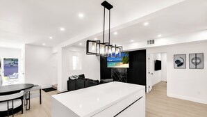 Een moderne keuken met een wit kookeiland, zwart hanglampen en een grote flatscreen televisie aan de muur.