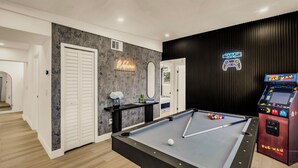Een pooltafel met een enkele witte bal, een neonbord waarop 'Gaming Zone' staat en een Pac-Man spelautomaat.