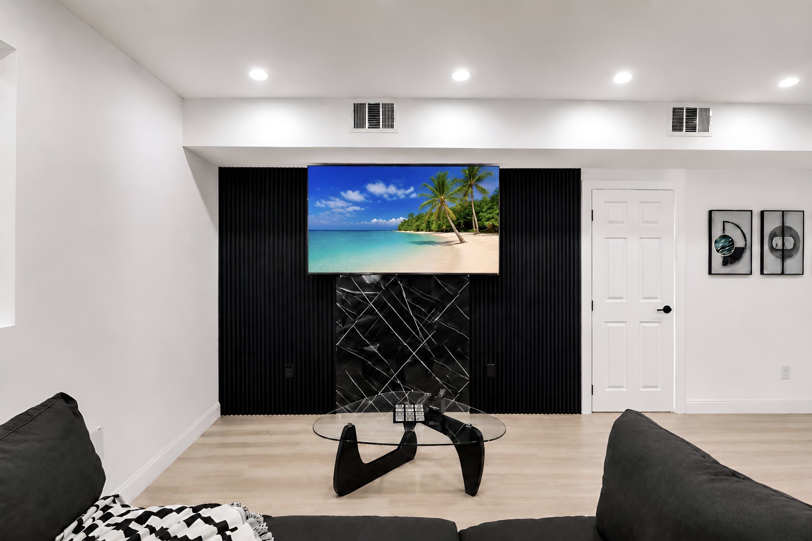 Un salon moderne avec un téléviseur à écran plat fixé sur un mur noir, une table basse en verre et une porte blanche.