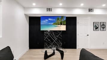 Un salon moderne avec un téléviseur à écran plat fixé sur un mur noir, une table basse en verre et une porte blanche.