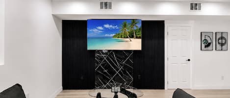 A modern living room with a flat-screen TV mounted on a black wall, a glass coffee table, and a white door.