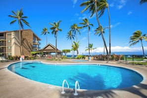 Ein Hotelpool mit Palmen, ein Gebäude mit Naturstein-Fassade und Blick auf den Ozean.