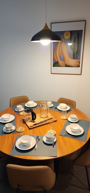 Ein runder Esstisch mit Geschirr, Besteck und einer Karaffe, gedeckt für eine Mahlzeit.