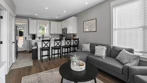 A modern kitchen with white cabinets, a dining area with a gray sofa, and a black coffee table.