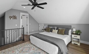 Un dormitorio con una cama, mesitas de noche, un ventilador de techo, una puerta y una escalera.