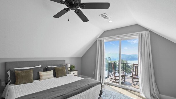 A bedroom with a bed, a ceiling fan, a nightstand, and a view of a balcony with a railing.