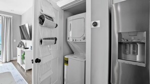 A modern kitchen with a stainless steel refrigerator, a built-in washer and dryer, and a flat-screen TV mounted on the wall.