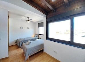 Ein Schlafzimmer mit zwei Betten, einem Deckenventilator, einem Fenster mit Aussicht und Holzboden.