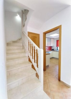 Eine Treppe mit weißen Balustraden führt zu einer Empore, einer Holztür und einem Blick in einen Küchenbereich mit weißen Schränken und einem roten Gerät.