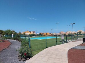 A swimming pool area with a fenced deck, a pathway, and a view of residential buildings in the background. - Welcome, EstrellaMarina, to Corralejo, Fuerteventura! (Geafond)