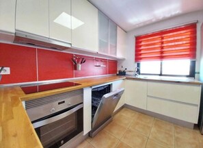 A kitchen with white cabinets, a red backsplash, a wooden countertop, a built-in oven, and a dishwasher. - Welcome, EstrellaMarina, to Corralejo, Fuerteventura! (Geafond)