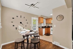 A dining area with a wall clock, a ceiling light fixture, and a kitchen in the background. - Chic 2BR Oasis - Downtown Birmingham (Birmingham)