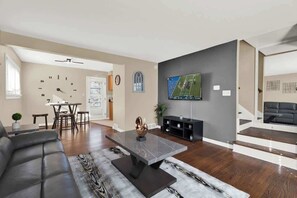 A modern living room with a flat-screen TV, a leather sofa, a marble coffee table, and a dining area with a white table and chairs. - Chic 2BR Oasis - Downtown Birmingham (Birmingham)