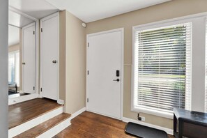 A hallway with a wooden floor, white doors, and a window with blinds. - Chic 2BR Oasis - Downtown Birmingham (Birmingham)