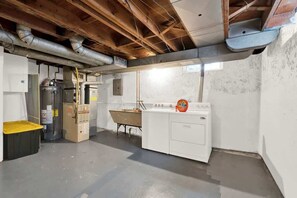 Ein Kellerraum mit freiliegenden Holzbalken, einer Waschmaschine und einem Technikraum mit Warmwasserbereiter.