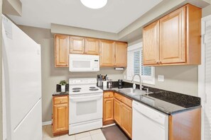 A kitchen with wooden cabinets, a white stove, a microwave, and a sink. - Lux 2BR-Downtown Birmingham (Birmingham)