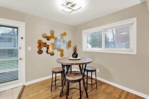 A dining area with a round table and four stools, a wall-mounted hexagonal light fixture, and a window with blinds. - Lux 2BR-Downtown Birmingham (Birmingham)