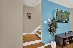 A staircase leading to a room with a blue wall, a flat-screen TV mounted above a dark wooden cabinet, and a potted plant. - Lux 2BR-Downtown Birmingham (Birmingham)