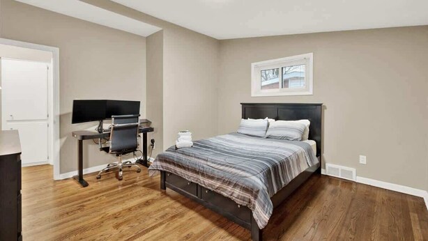 Une chambre à coucher avec un lit, un bureau avec un ordinateur et une fenêtre.