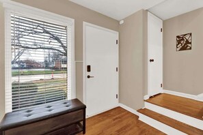 Ein Zimmer mit einer Bank, einer weißen Tür und Blick durch ein Fenster mit Jalousien.