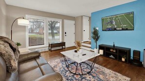 Un salon comprenant un canapé, une table basse, un téléviseur fixé au mur et un escalier menant à un autre niveau.
