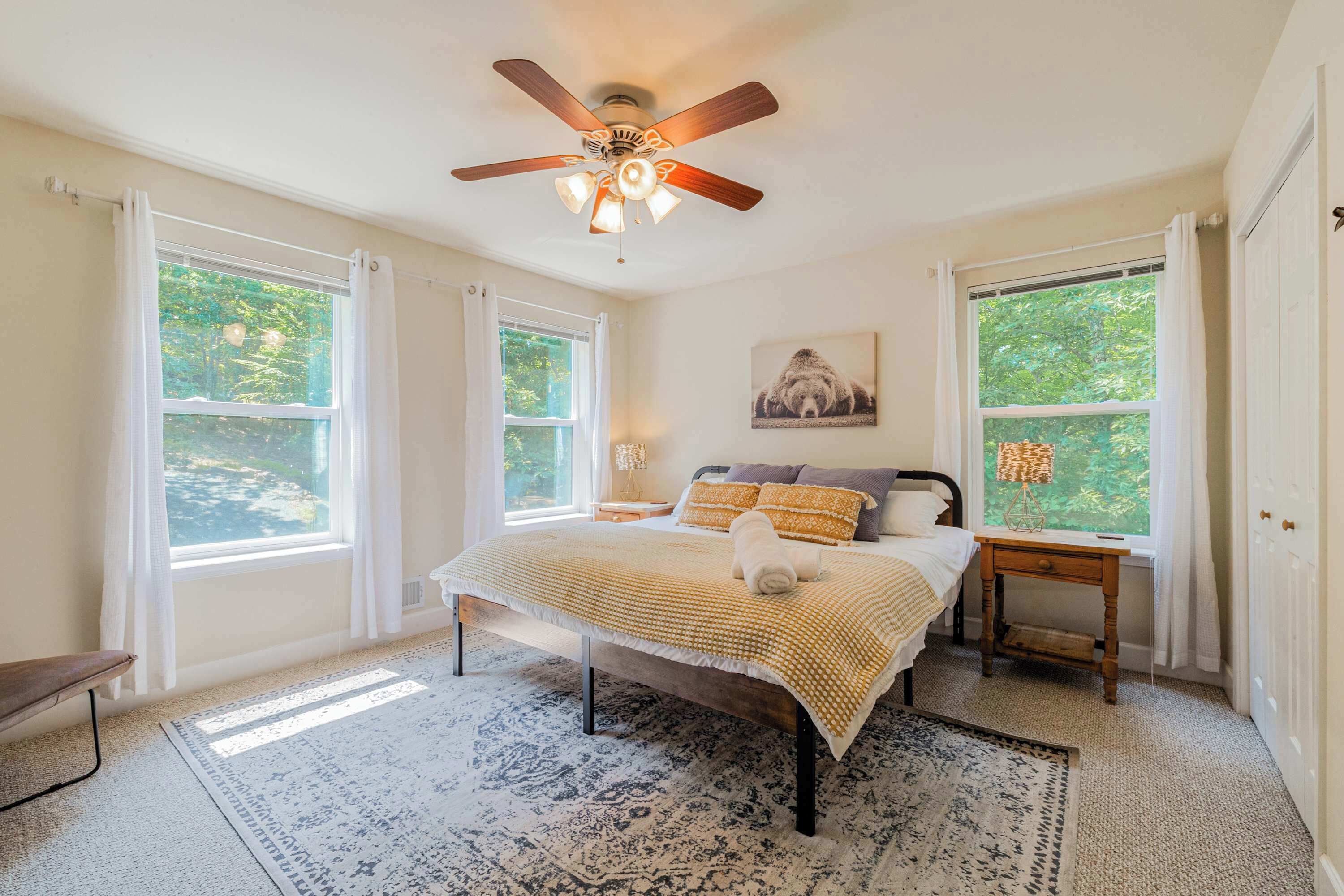 A bedroom with a bed, a nightstand, a ceiling fan, and two windows.