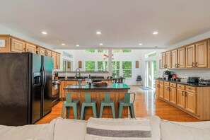 A spacious kitchen with wooden cabinets, a large island with bar stools, and a black refrigerator.