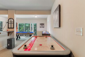 A room with a foosball table, a pool table, and a large window providing a view of trees.