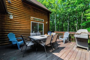 A wooden cabin with a deck, outdoor seating, and a grill.