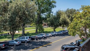 Un estacionamiento con coches y árboles, una zona verde y un edificio al fondo.