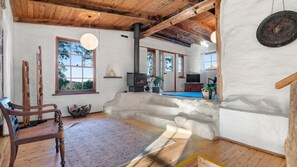 A rustic interior with a stone fireplace, wooden beams, and a large window. - The Cottage at Indooroopilly (Bellawongarah)