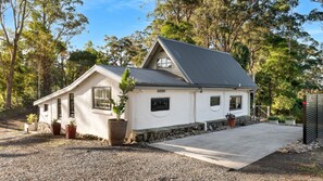 A single-story house with a sloped roof, a front porch, and a gravel driveway. - The Cottage at Indooroopilly (Bellawongarah)